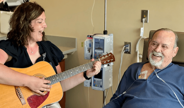 Woman with Healing Arts program playing guitar for patient